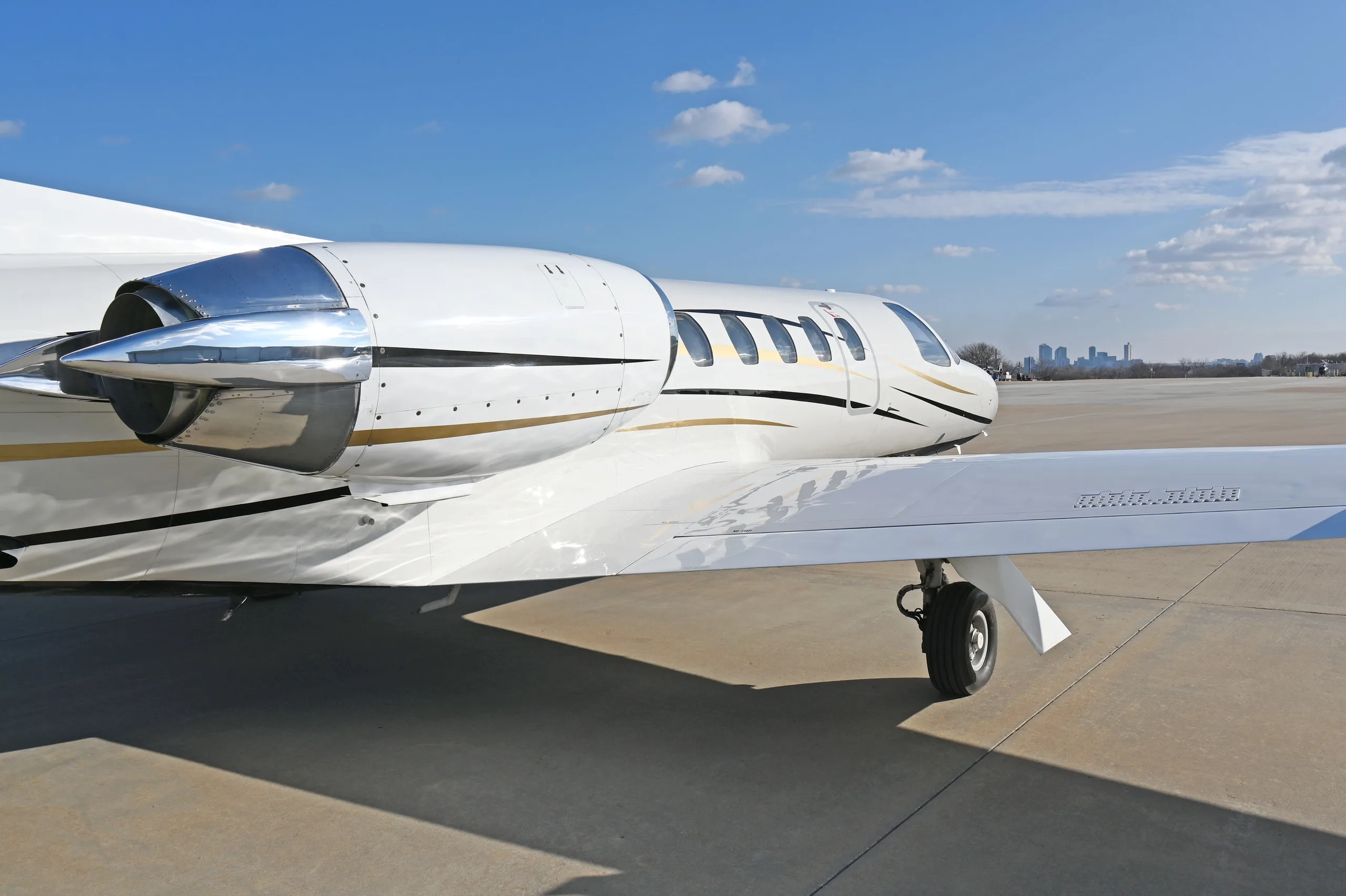 A close-up view of the right wing and engine of a white business jet with a city skyline in the distance.