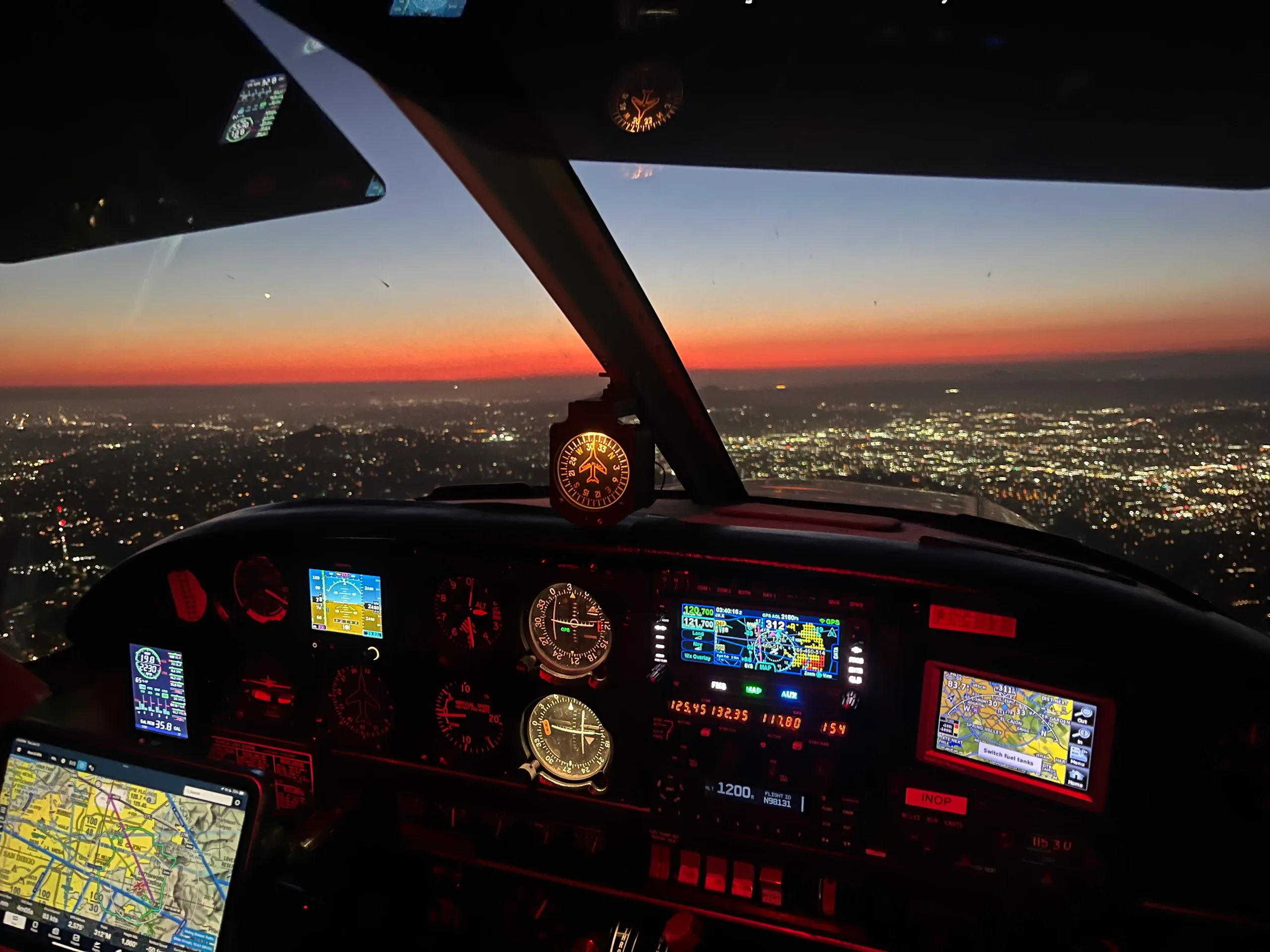 The cockpit of an aircraft at dusk, showing the instrument panel and city lights below.