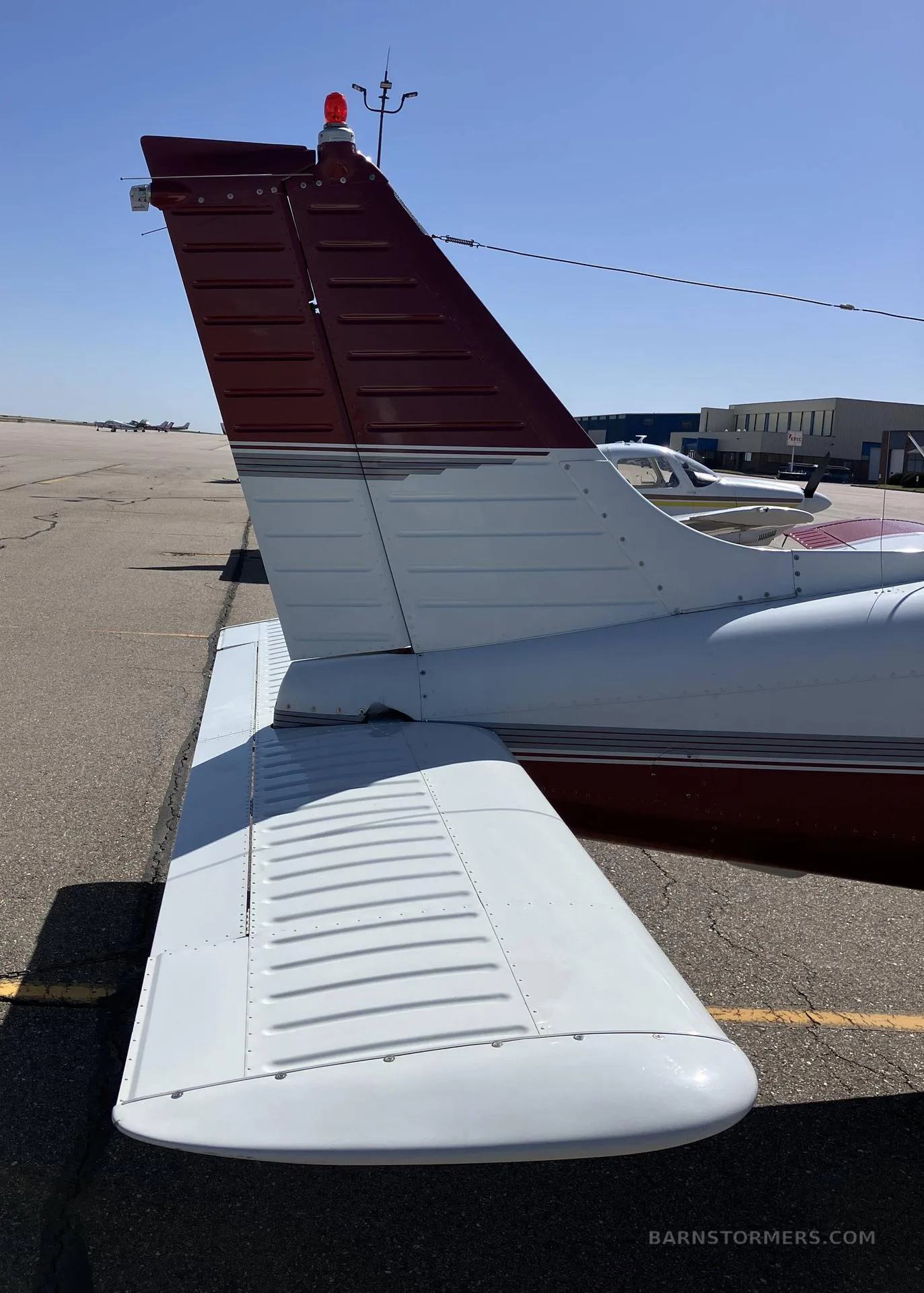 A close-up view of the white and maroon tail and right wing of a Piper Arrow aircraft.