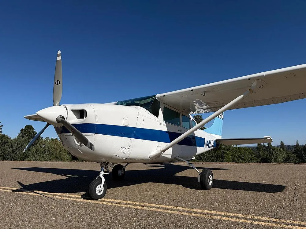 A front-left view of the white and blue single-engine aircraft N3746, showing its propeller and landing gear on an asphalt surface.