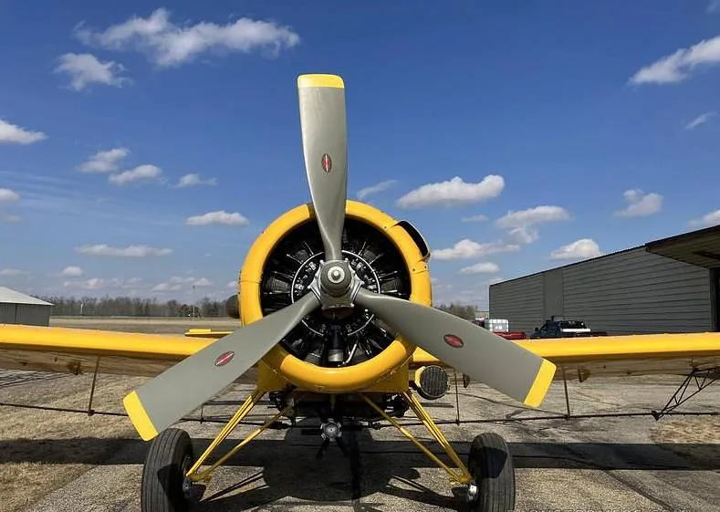 A head-on view of a yellow agricultural aircraft, featuring its large propeller and radial engine.