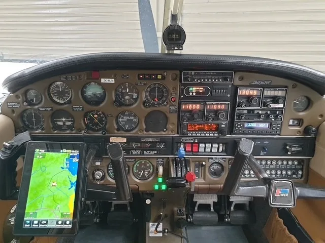 The cockpit of a Piper aircraft showing the instrument panel, controls, and a tablet mounted on the yoke.