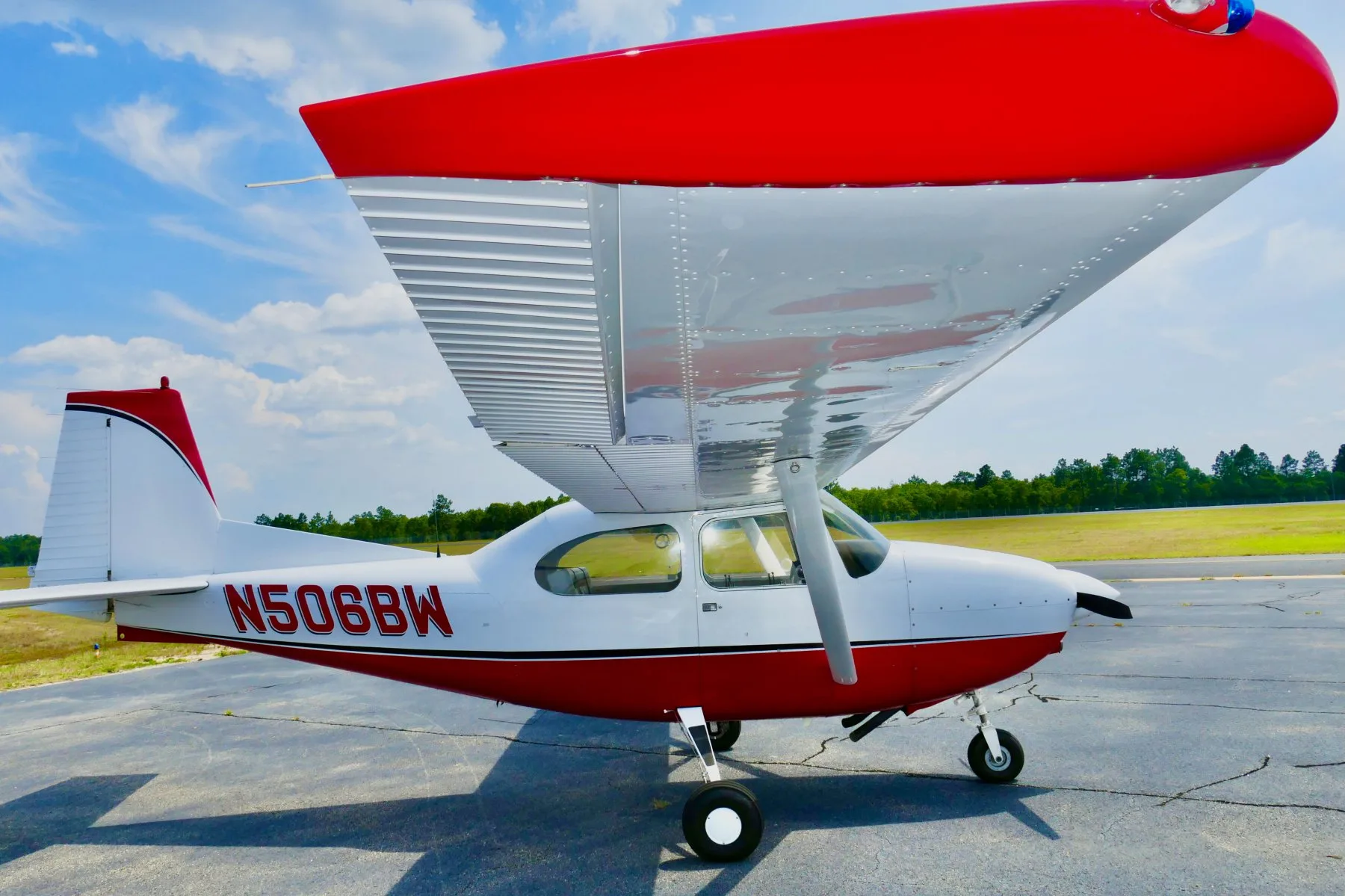 A low-angle side-right view of a white and red Cessna 172 aircraft, N506BW, showing the underside of the wing.
