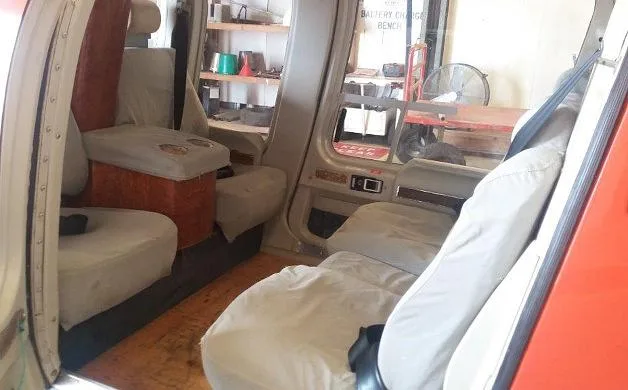 The beige interior cabin of a helicopter, showing two passenger seats and a storage area in the background.