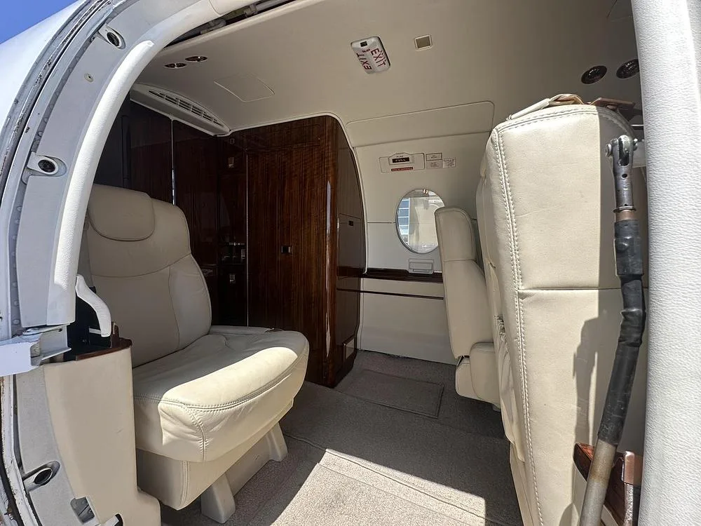 The interior cabin entrance of a business jet, showing beige leather seats and wood paneling.