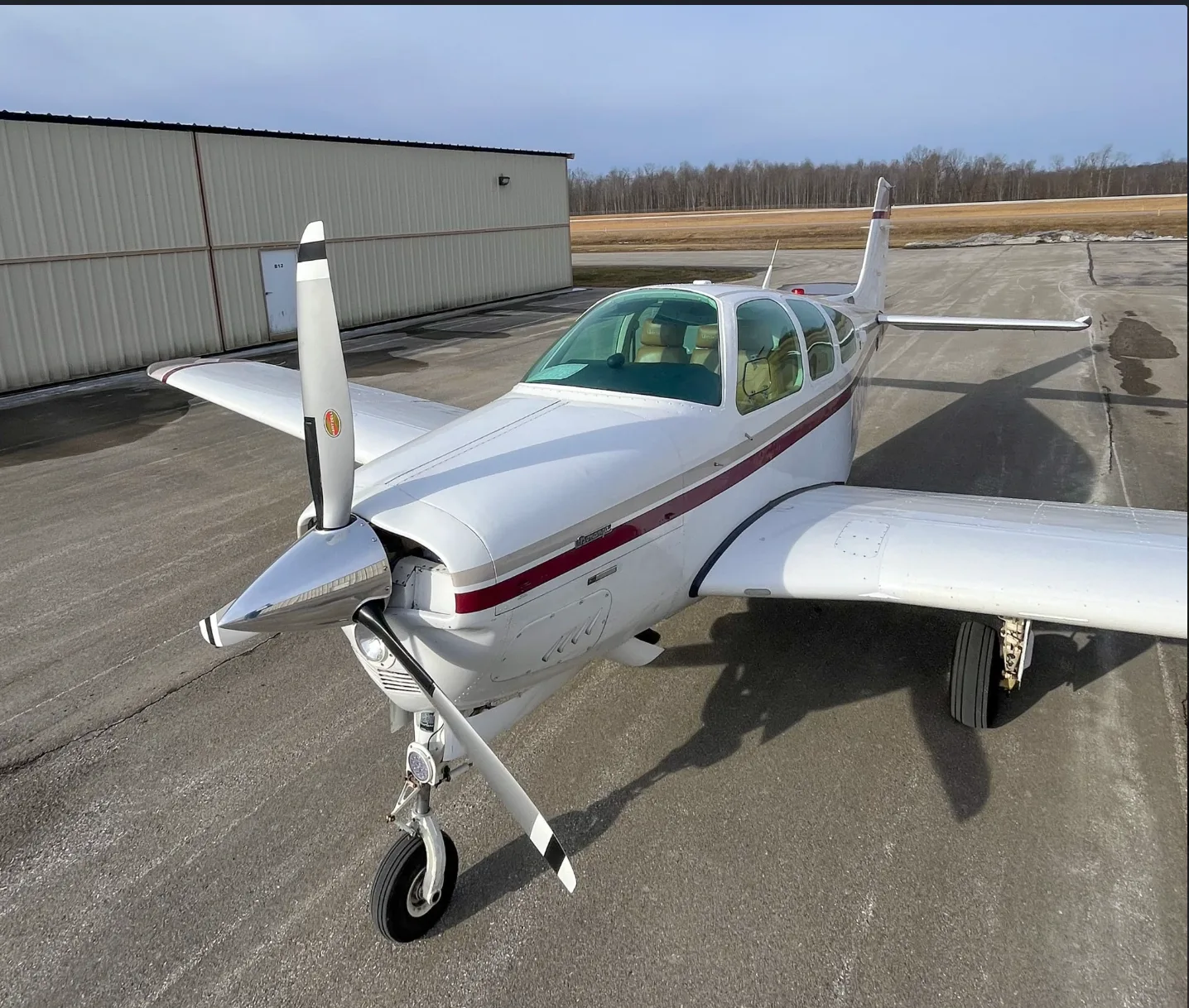An elevated front-quarter view of a white and maroon Beechcraft Bonanza aircraft on a tarmac.