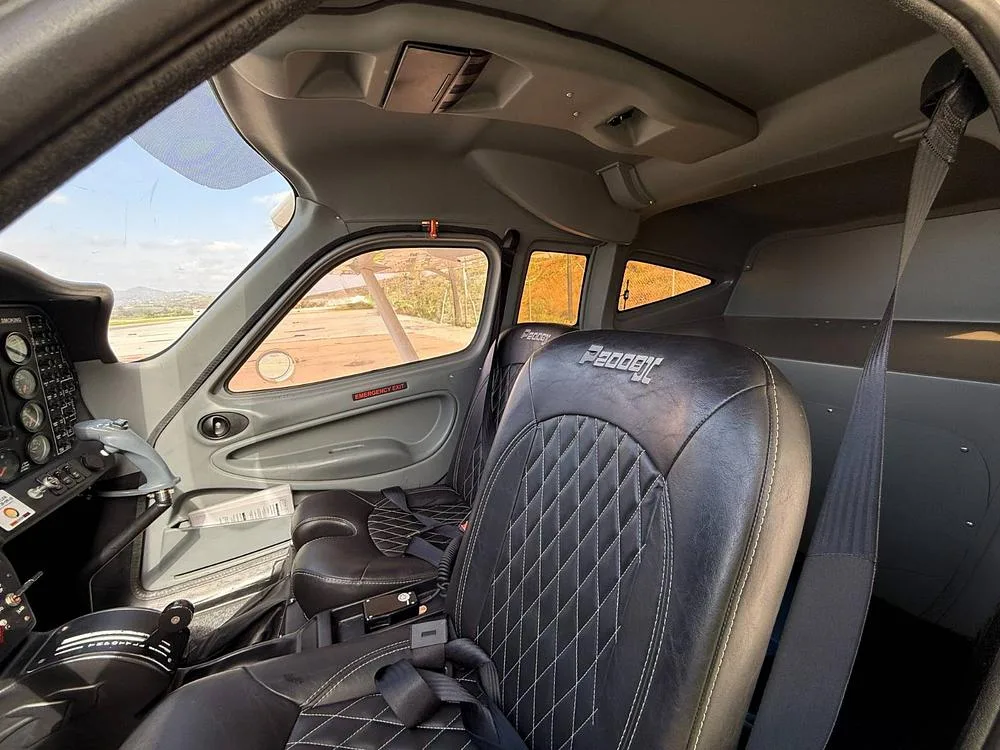 The interior cabin of a Tecnam P2008, showing black leather seats with white stitching and the side panel.
