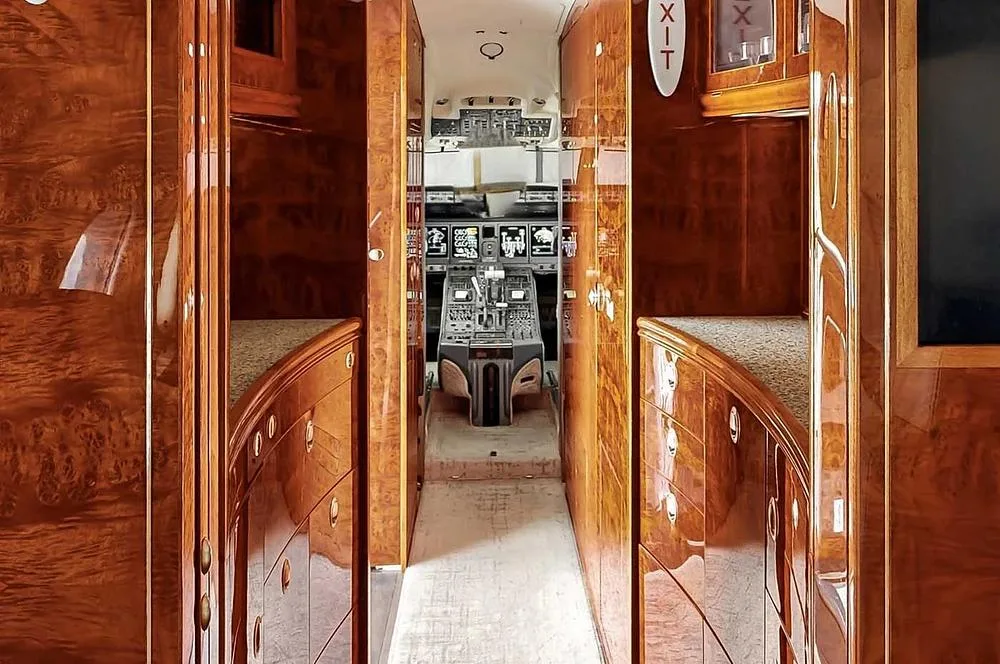A view looking through a wood-paneled galley or corridor into the cockpit of a private jet.