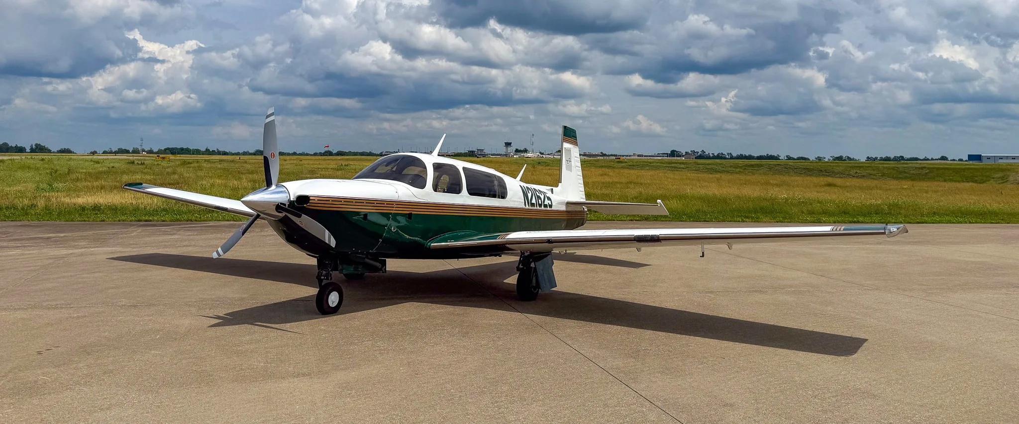 A white and green Mooney M20 aircraft with registration N21625 parked on an airfield under a cloudy sky.