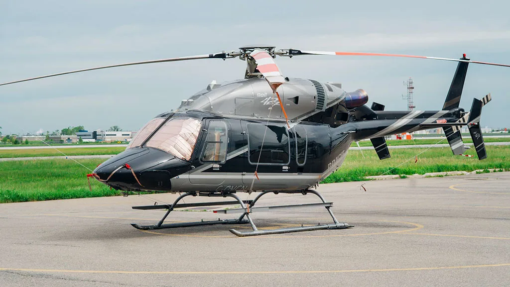 A black and silver Bell 427 helicopter with sunshades on the windshield, parked on an airfield.
