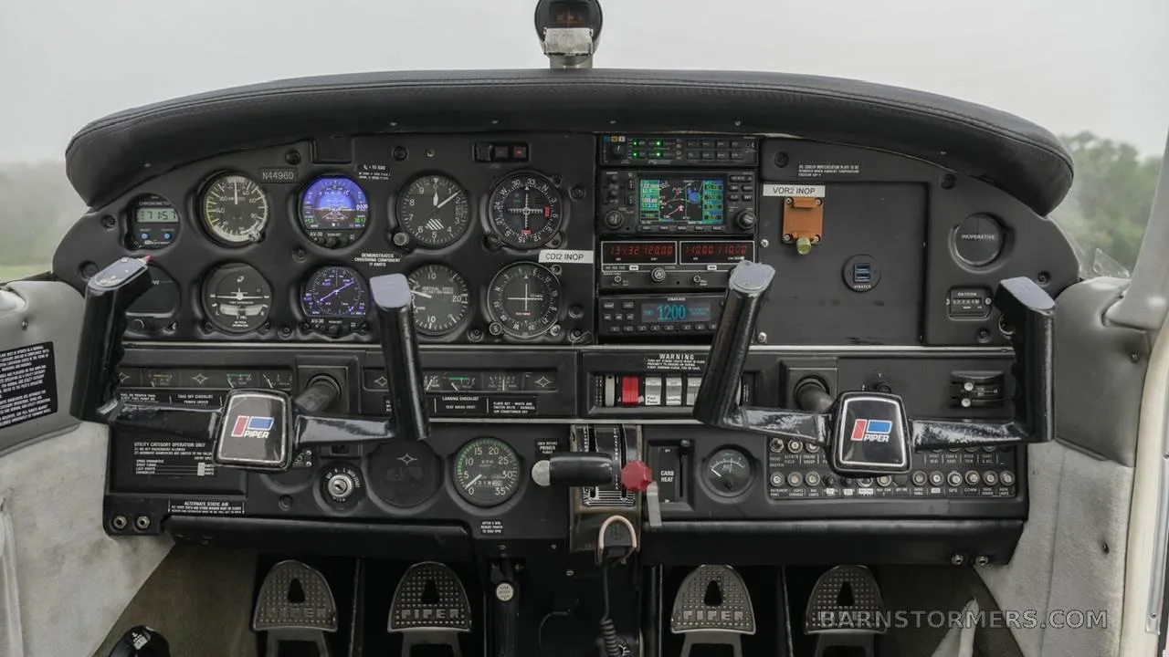 The cockpit of a Piper PA-28 series aircraft, showing the instrument panel with analog gauges and modern avionics, and two control yokes.