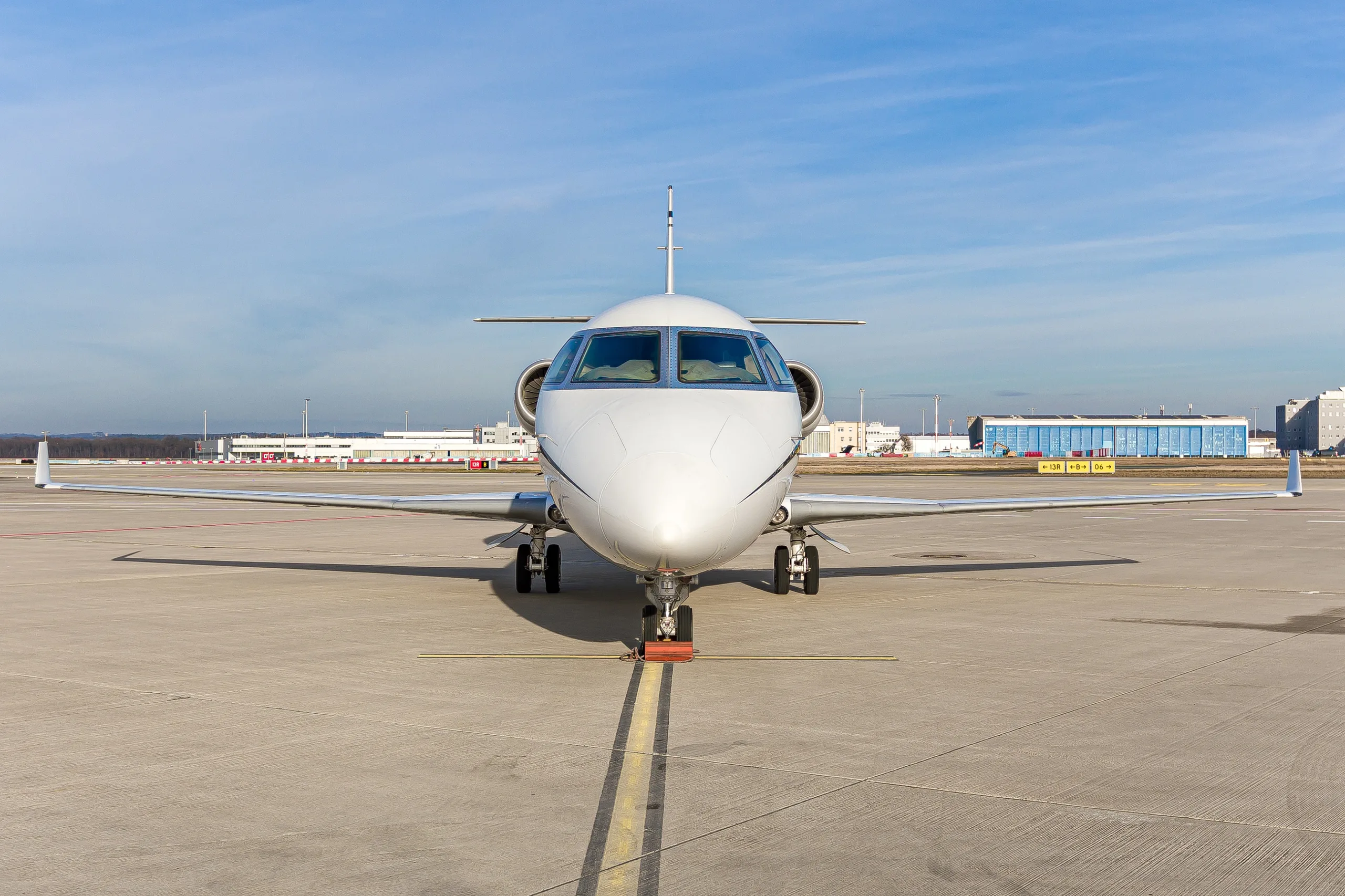 A white Gulfstream G200 business jet parked head-on on an airport tarmac under a clear blue sky.