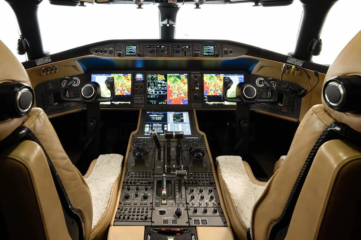 The modern cockpit of a business jet features multiple digital displays and tan leather pilot seats.