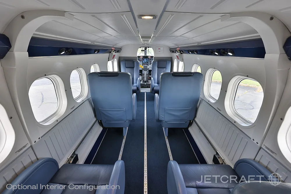 A view down the aisle of an aircraft cabin with blue seats and the cockpit visible in the distance.