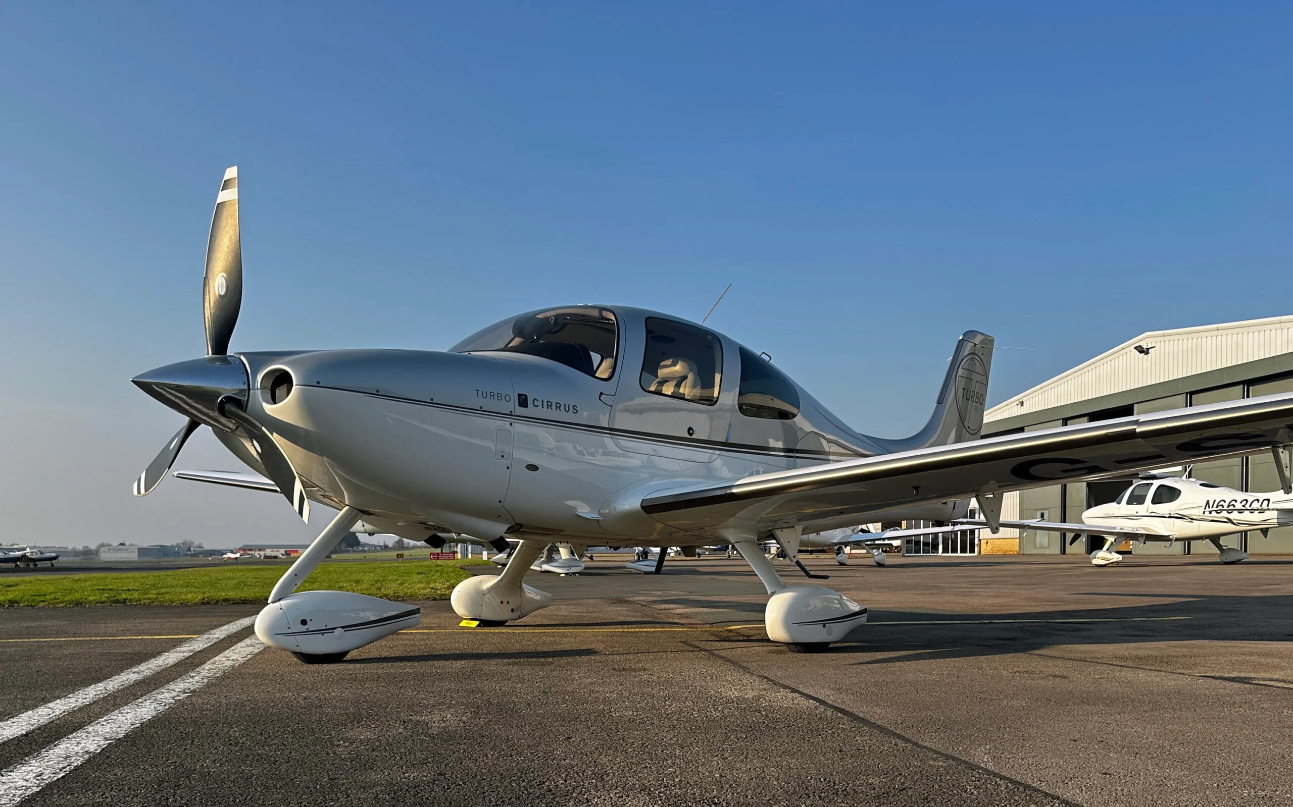 A silver and white Cirrus SR22 Turbo aircraft with registration G-SRZZ parked on an airfield.