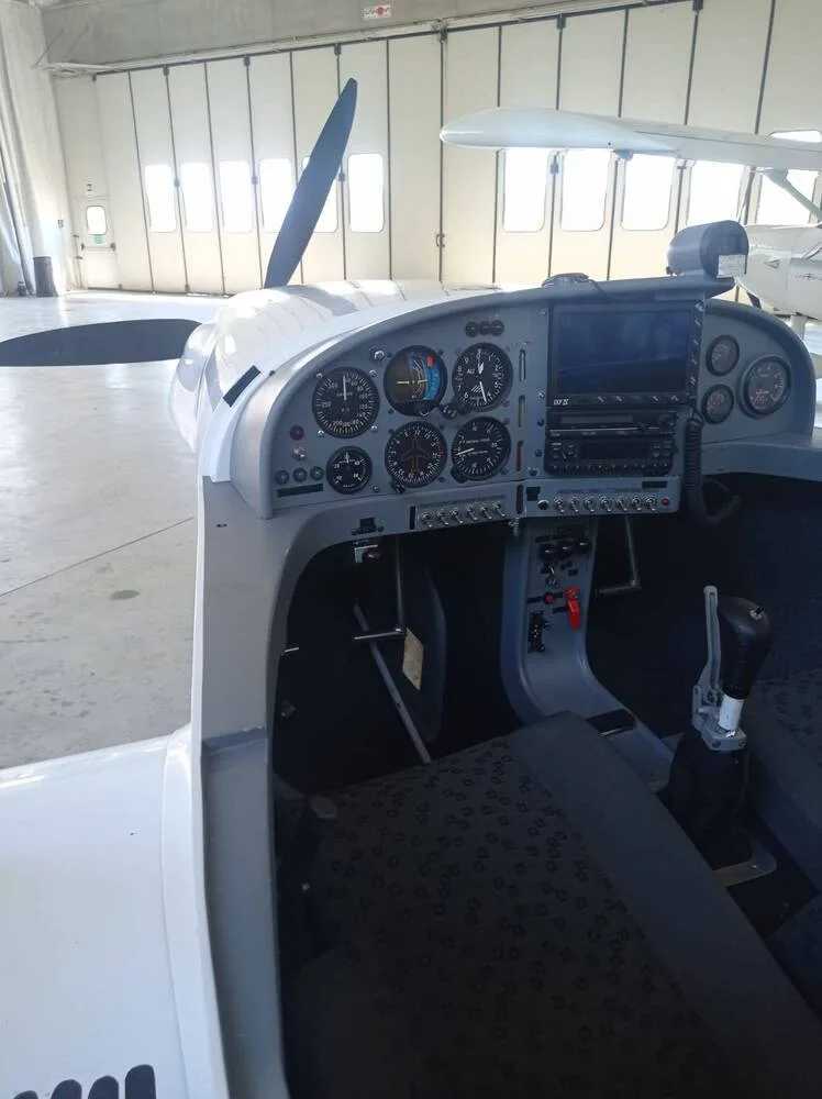 The cockpit of an ultralight aircraft, showing the instrument panel with analog gauges and a digital display, along with the control stick.