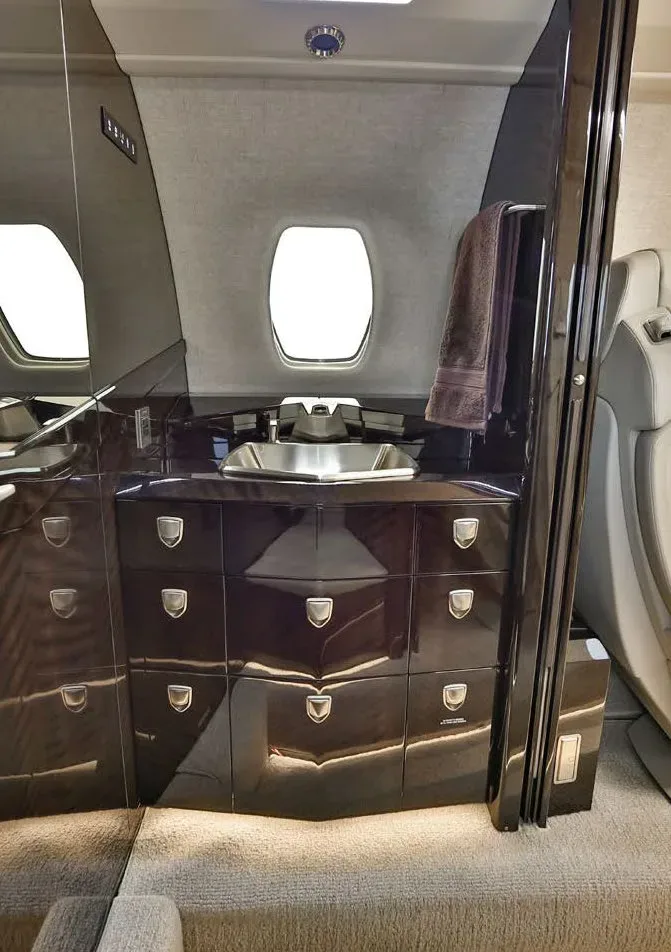 A modern aircraft lavatory or galley area featuring a sink, dark cabinetry, and a small window.