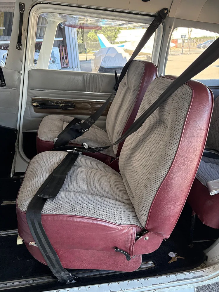 The front and rear seats of the aircraft cabin, upholstered in grey fabric with red trim.