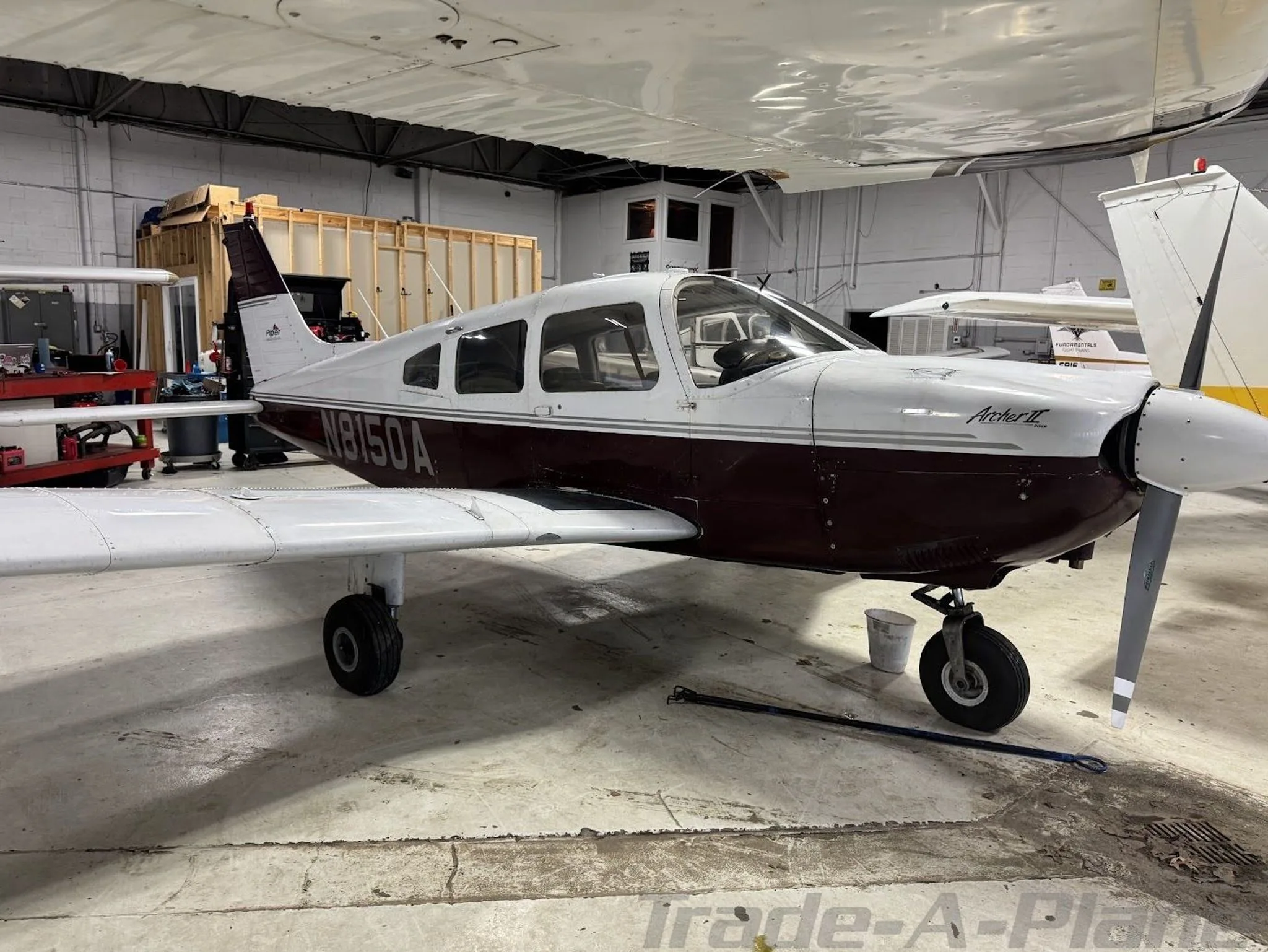 A white and maroon Piper Archer II (N8150A) parked in a hangar, viewed from the front-left.