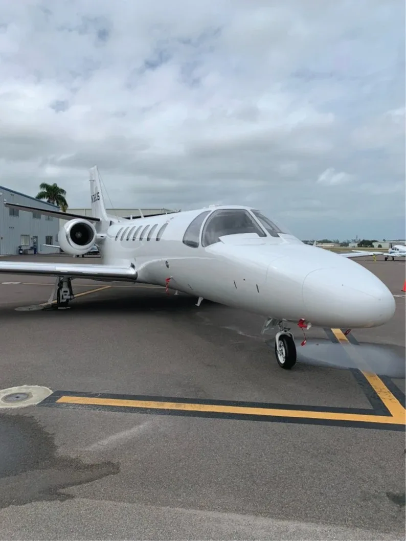 A white Cessna Citation business jet (N768JS) is parked on an airport tarmac, viewed from the front-right.