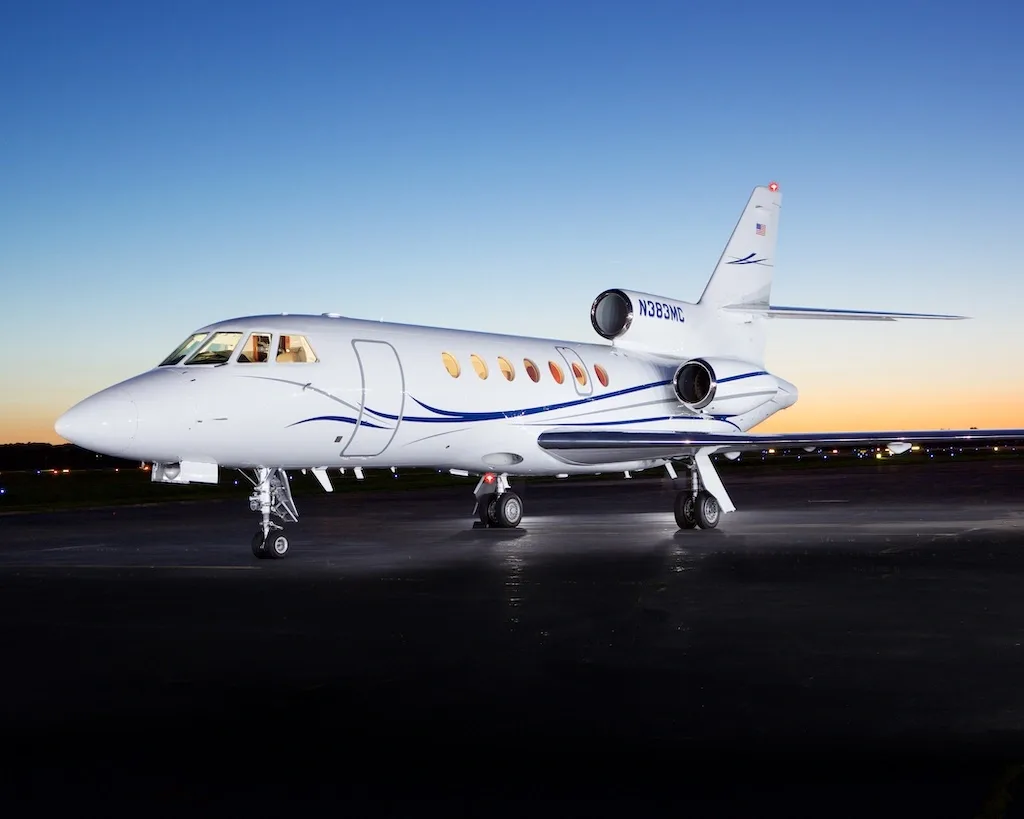 A white business jet, N383MC, with blue and grey stripes, parked on a tarmac at dusk, viewed from a slightly different angle.