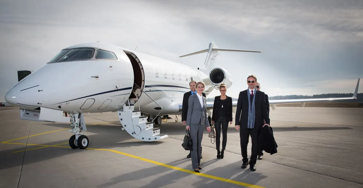 Business professionals walking away from a white private jet with its stairs extended on an airport tarmac.
