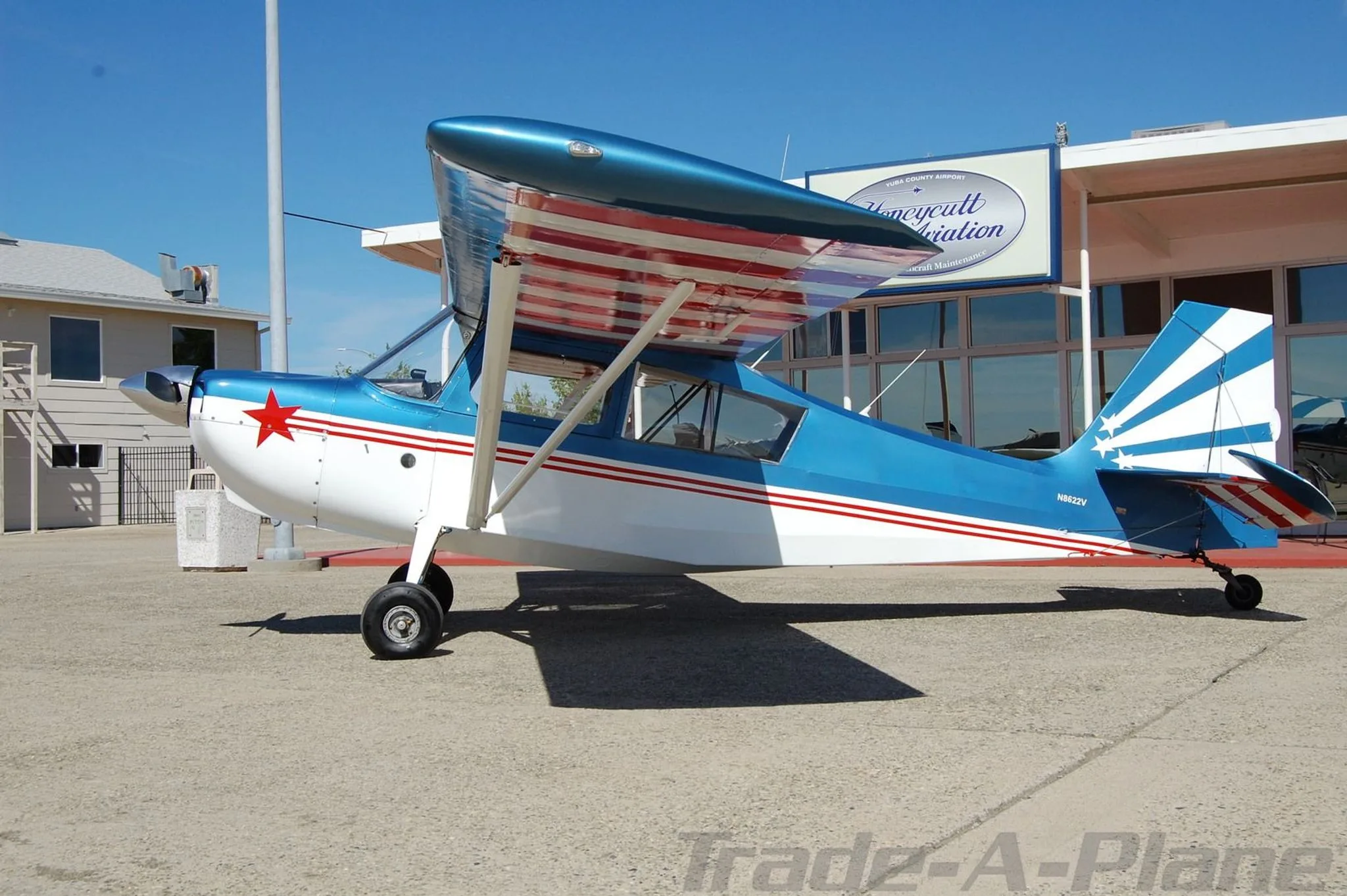 A side view of the blue, white, and red single-engine aircraft with N8622V registration, parked on an airfield next to a building.