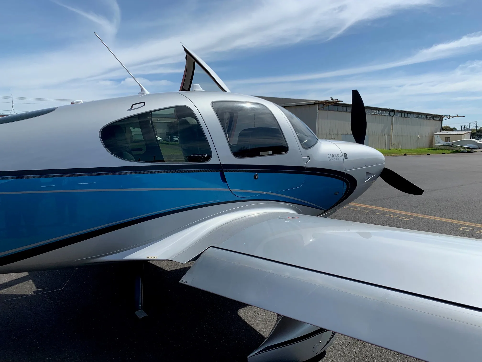 A side view of a silver and blue Cirrus SR22T aircraft with its door slightly ajar, parked on an airfield.
