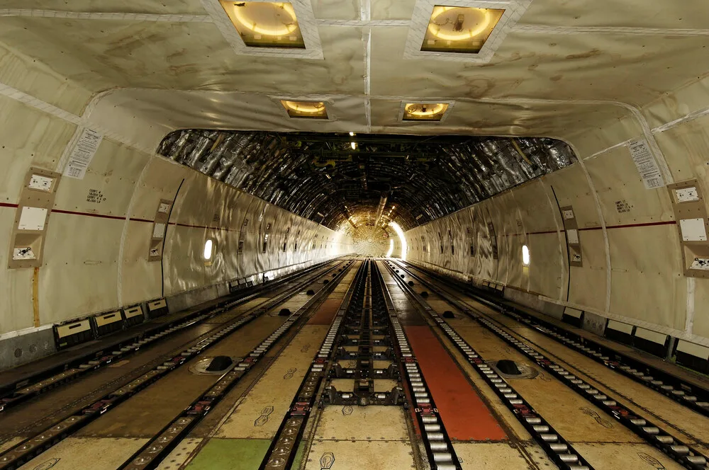 A long view down the empty cargo hold of an aircraft, showing multiple floor tracks and overhead lighting.