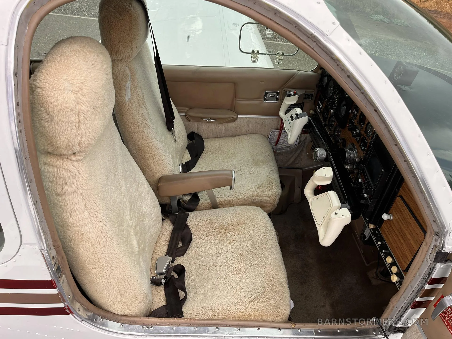 The front cabin of a Beechcraft Bonanza, showing two sheepskin-covered seats and part of the instrument panel through the open door.