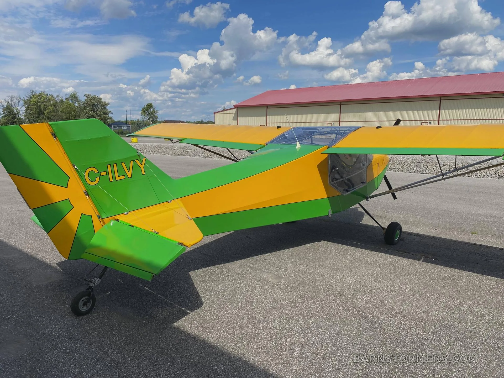 A rear-side view of a yellow and green high-wing aircraft with registration C-ILVY on the tail, parked on an airfield.