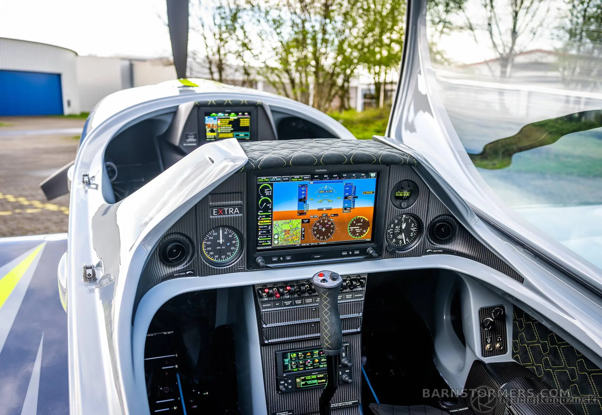 The cockpit of an Extra aircraft shows a modern glass panel with multiple displays and controls.