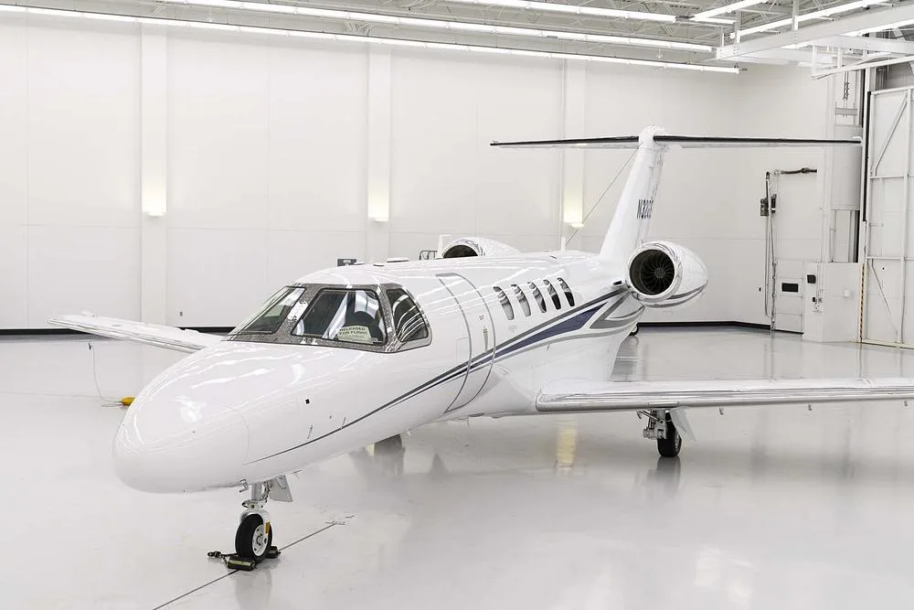 A front-left view of the white business jet N32GE with blue and grey stripes, parked in a hangar.