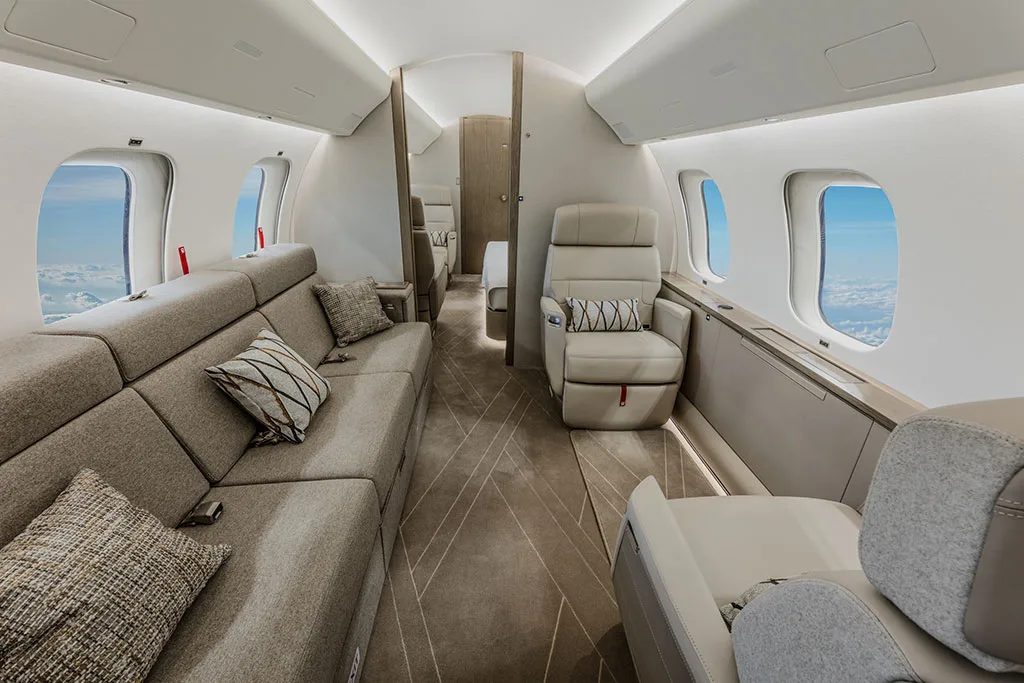 A private jet cabin with a long grey sofa on one side and individual beige seats on the other.