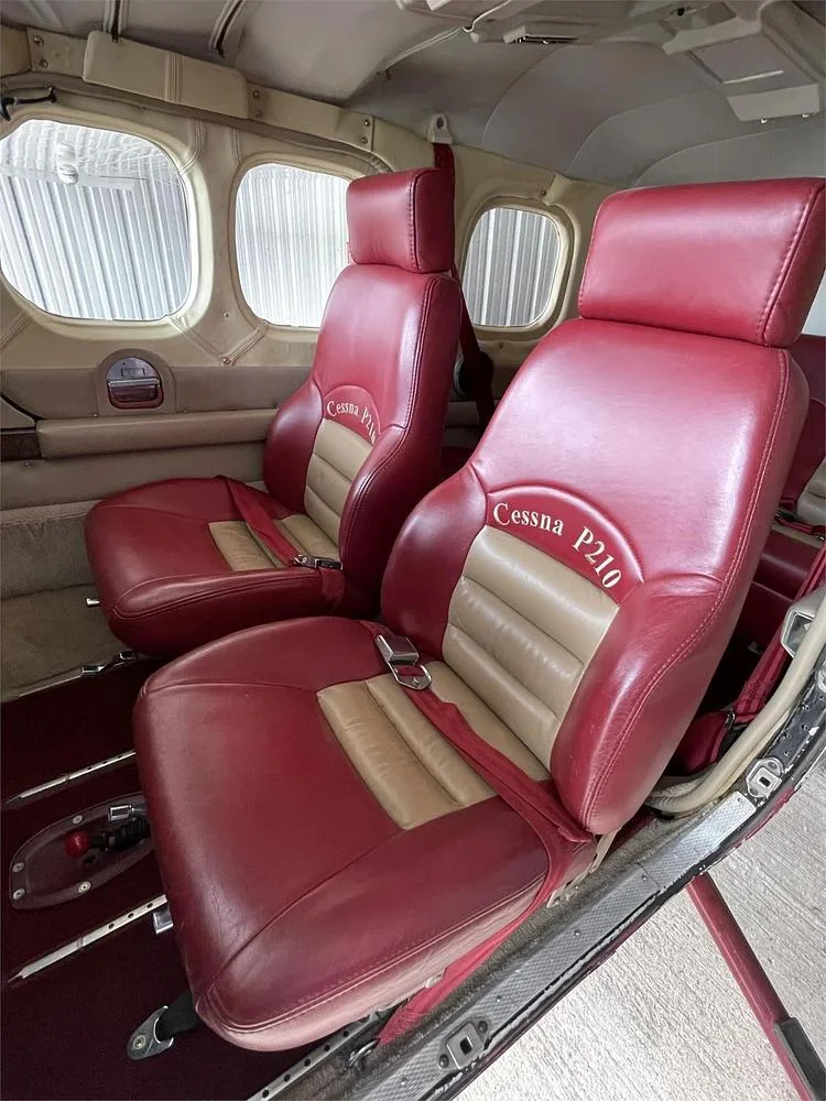 Two red and tan leather passenger seats in the cabin of a Cessna P210 aircraft.