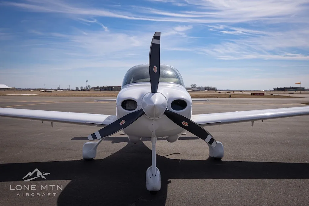 A head-on view of a white single-engine aircraft with a three-bladed propeller, tail number N924JT, parked on an airport tarmac.