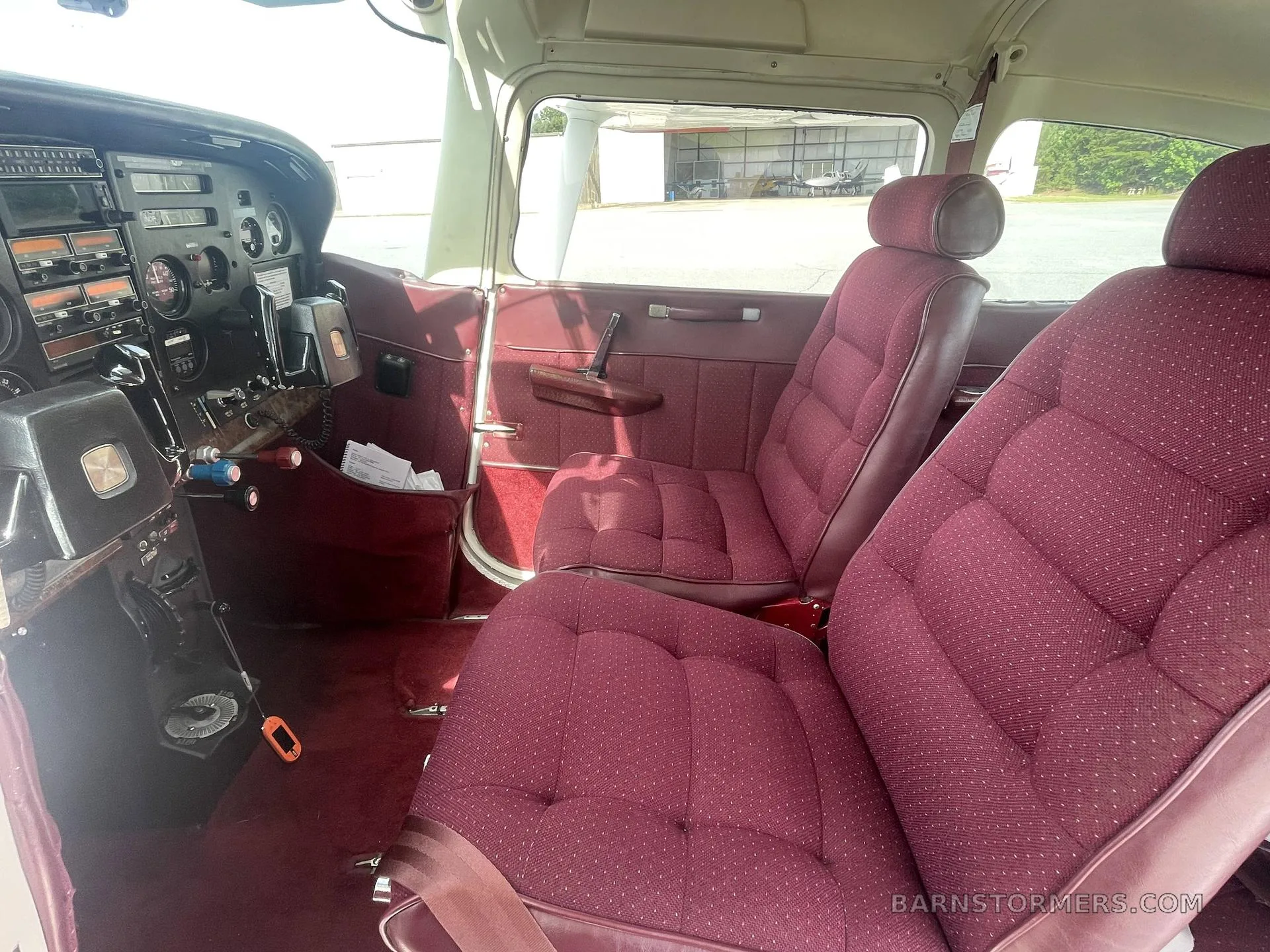 The front cabin of the aircraft features a maroon fabric passenger seat and a partial view of the cockpit instruments.