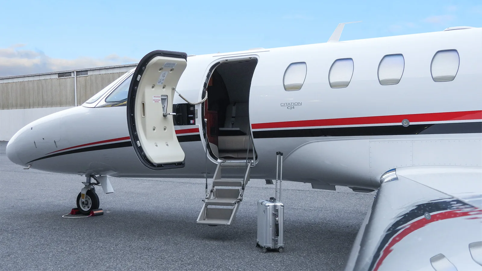 A close-up view of the open main cabin door and forward fuselage of a white Citation CJ4 business jet, showing "CITATION CJ4" text and a suitcase.