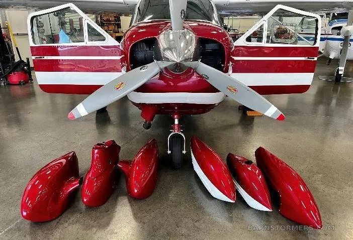 The front of a red and white aircraft in a hangar with its engine cowling open and red wheel fairings on the floor.
