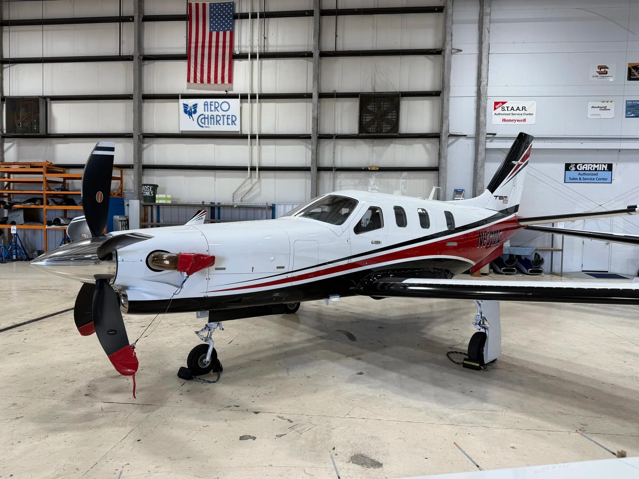 A white, red, and black TBM 930 turboprop aircraft is parked inside a hangar.