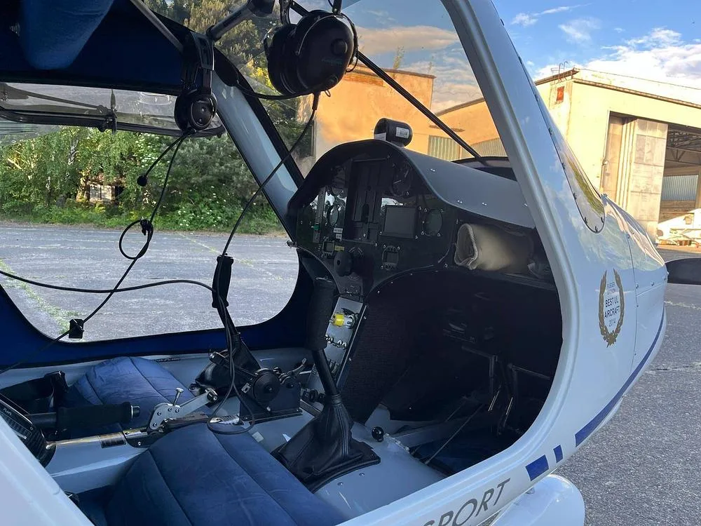 View into the cockpit of an Alpha Light Sport aircraft, showing the instrument panel, controls, and blue seats with an open canopy.