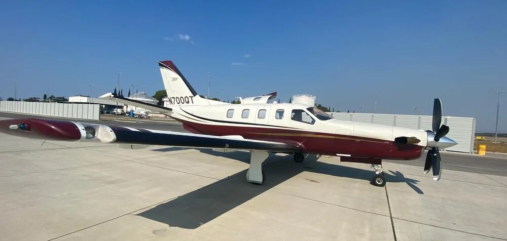 A white and maroon single-engine turboprop aircraft parked on an airfield under a clear blue sky.