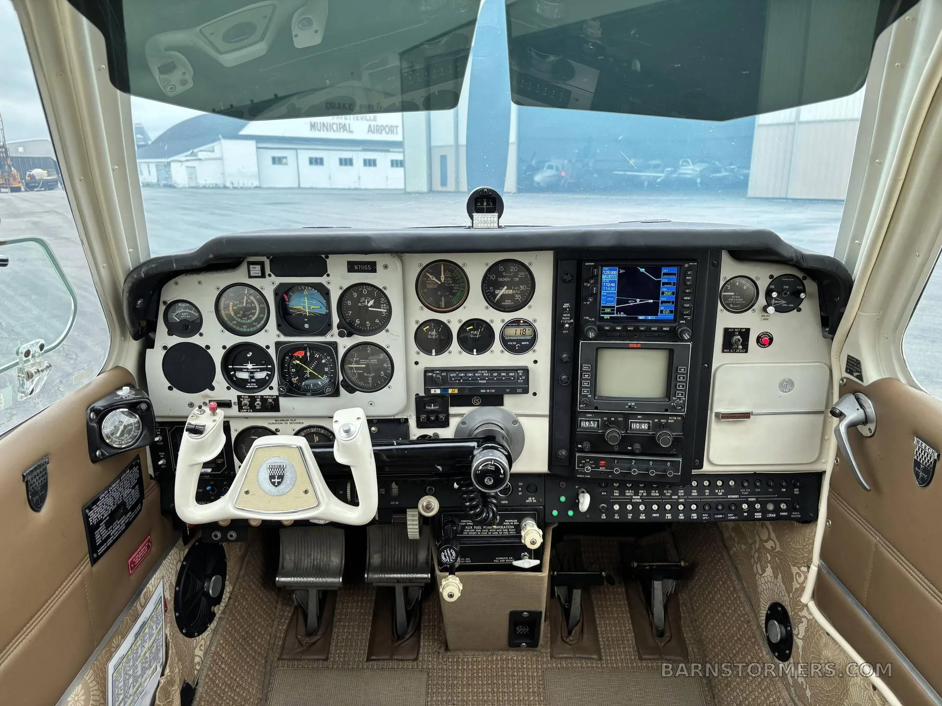 The cockpit of a light aircraft with analog gauges, modern avionics, and a white yoke.