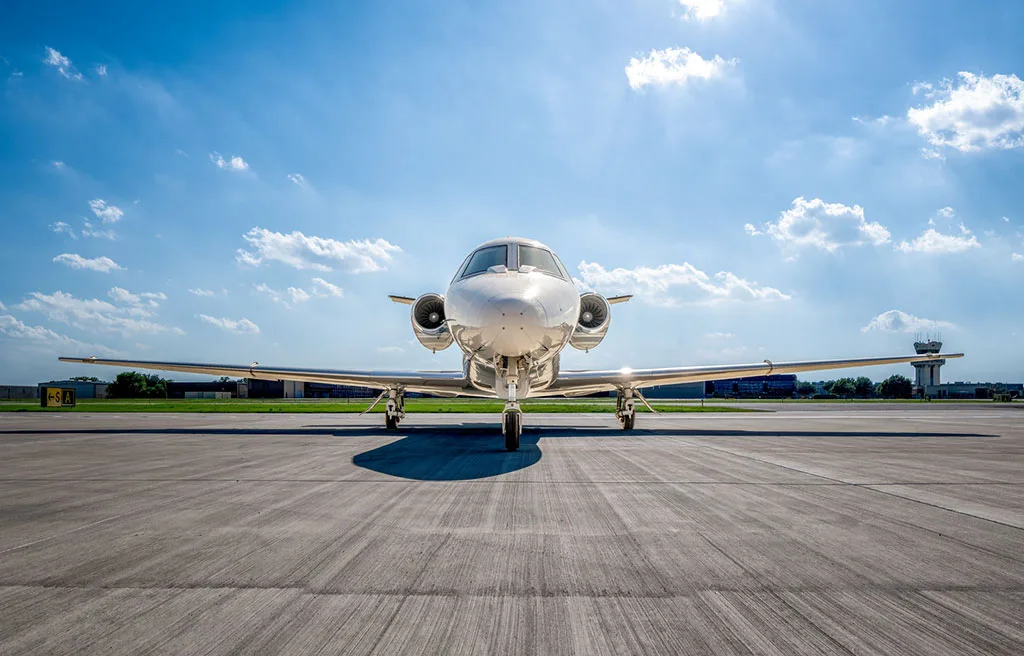 A head-on view of the Cessna Citation Latitude business jet, N8701L, on the tarmac with an air traffic control tower in the background.