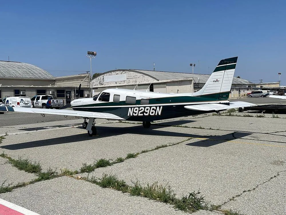 A Piper Saratoga II TC, registration N9296N, in dark green and white, parked on an airfield with buildings in the background.