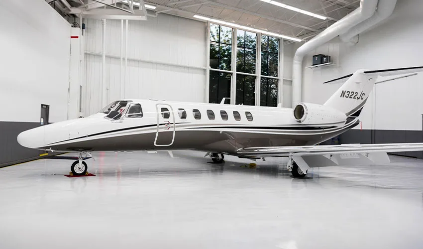A white and grey business jet with registration N322JC is parked inside a brightly lit hangar.
