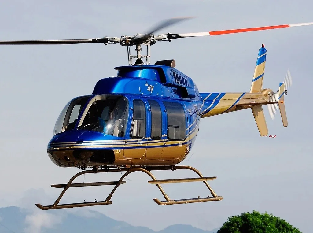 A blue and gold helicopter flies against a light blue sky with distant mountains.