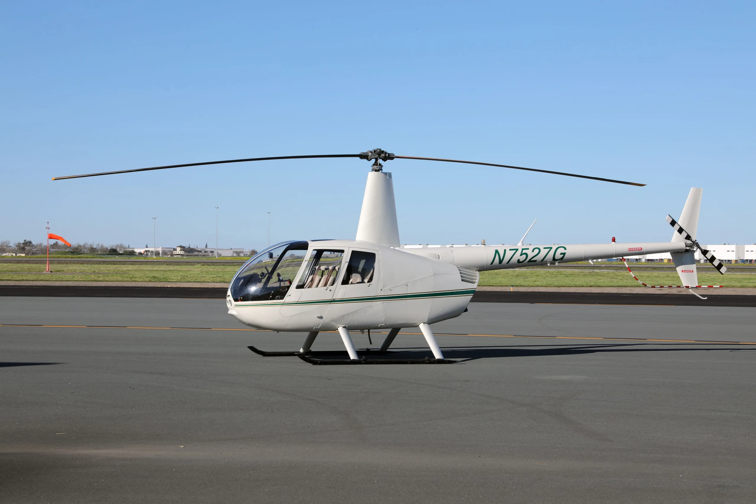 White Robinson R44 Raven II helicopter with a green stripe, registration N7527G, parked on an airfield.