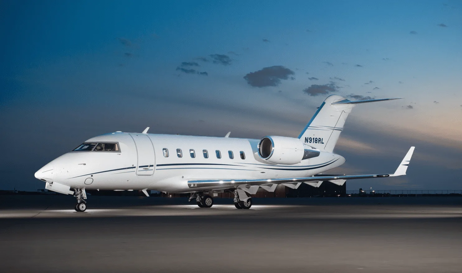 A white Bombardier Challenger business jet with blue accents on the tail, registration N918RL, parked on a tarmac at dusk.
