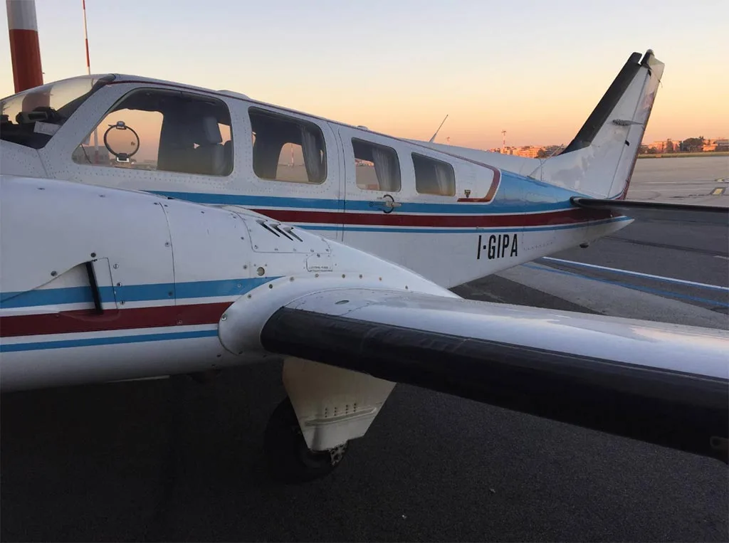 A white twin-engine aircraft with blue and red stripes on the tail and fuselage, registration I-GIPA, parked on an airfield at sunset.